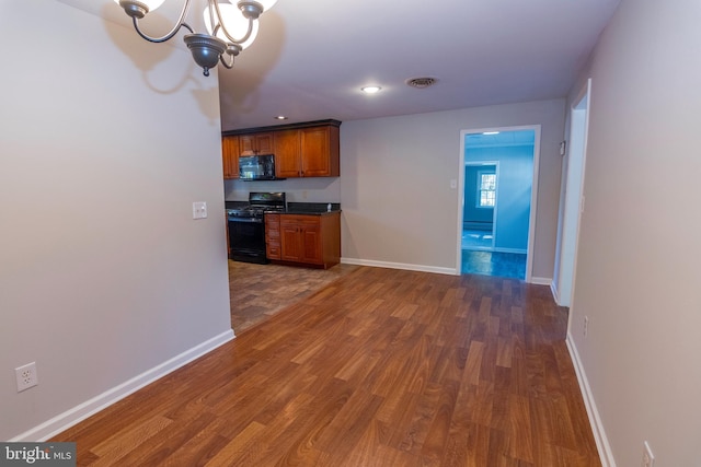 kitchen featuring range with gas cooktop, visible vents, brown cabinetry, black microwave, and wood finished floors