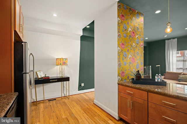 kitchen featuring pendant lighting, stainless steel refrigerator, light hardwood / wood-style flooring, and dark stone counters