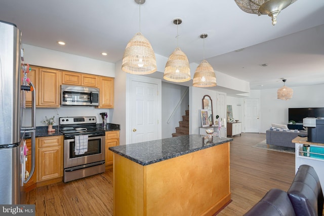 kitchen with decorative light fixtures, stainless steel appliances, light wood-type flooring, and dark stone counters