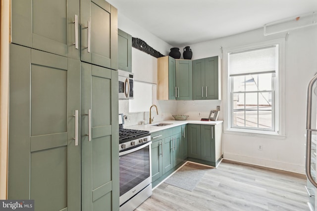 kitchen with sink, tasteful backsplash, green cabinetry, appliances with stainless steel finishes, and light hardwood / wood-style floors