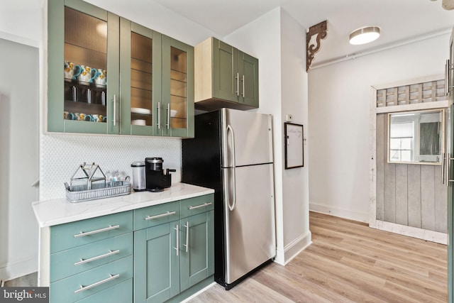 kitchen featuring light stone counters, tasteful backsplash, stainless steel refrigerator, green cabinets, and light wood-type flooring