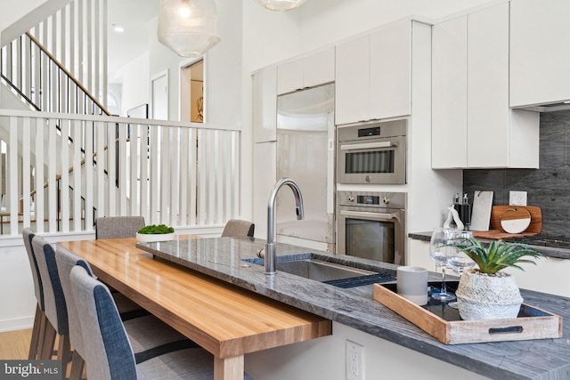 kitchen with light hardwood / wood-style floors, white cabinetry, backsplash, stainless steel appliances, and sink