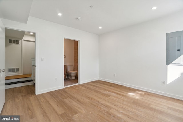 unfurnished bedroom featuring electric panel, light wood-type flooring, and ensuite bathroom