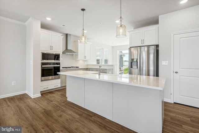 kitchen featuring stainless steel appliances, wall chimney range hood, white cabinetry, and a kitchen island with sink