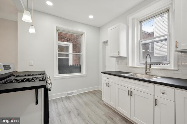 kitchen with white cabinets, hanging light fixtures, sink, stainless steel gas range, and backsplash