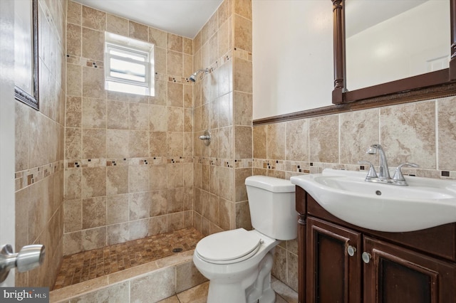 bathroom featuring a tile shower, vanity, tile walls, and toilet