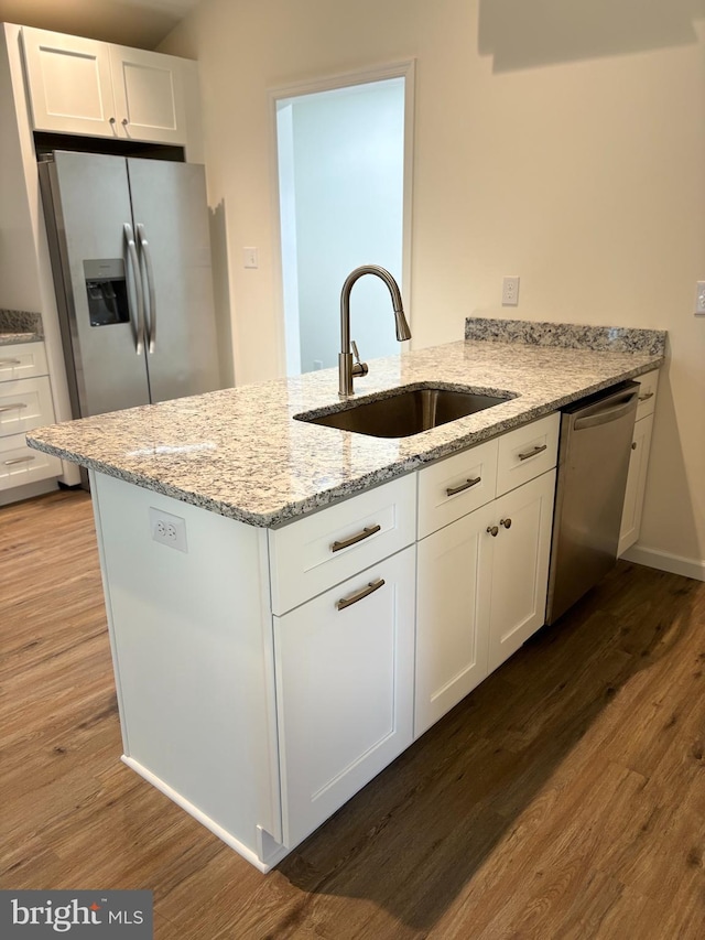 kitchen with sink, white cabinetry, stainless steel appliances, light stone countertops, and hardwood / wood-style floors