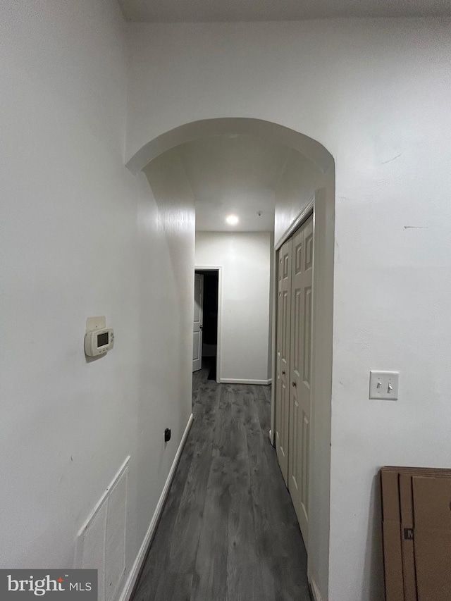 corridor featuring baseboards, wood finished floors, and arched walkways