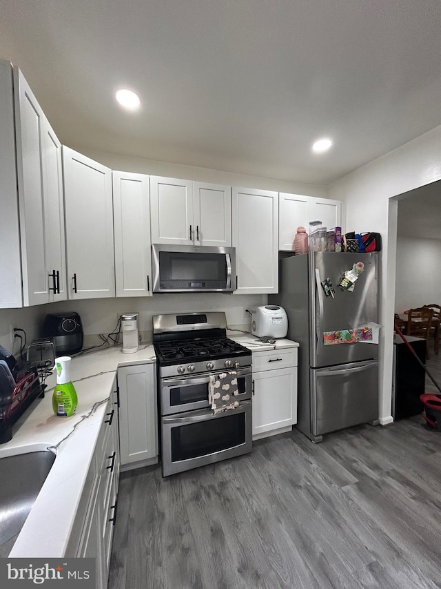 kitchen with appliances with stainless steel finishes, hardwood / wood-style floors, and white cabinetry