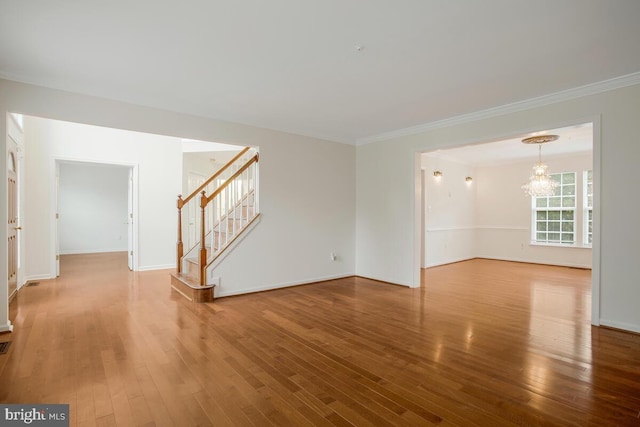 empty room featuring an inviting chandelier, wood-type flooring, and crown molding