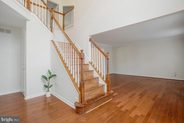 staircase featuring wood-type flooring, crown molding, and a towering ceiling