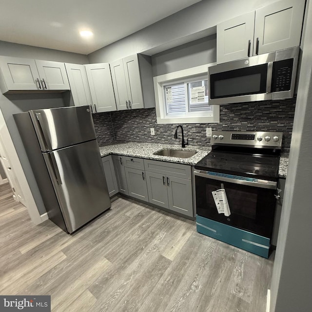 kitchen with tasteful backsplash, light stone countertops, sink, gray cabinets, and stainless steel appliances