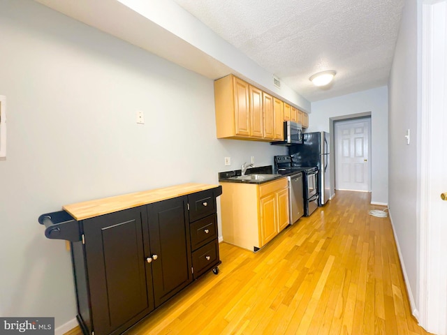 kitchen with light brown cabinets, stainless steel appliances, sink, light hardwood / wood-style flooring, and a textured ceiling