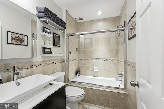 full bathroom featuring tile walls, shower / bath combination with glass door, toilet, and vanity