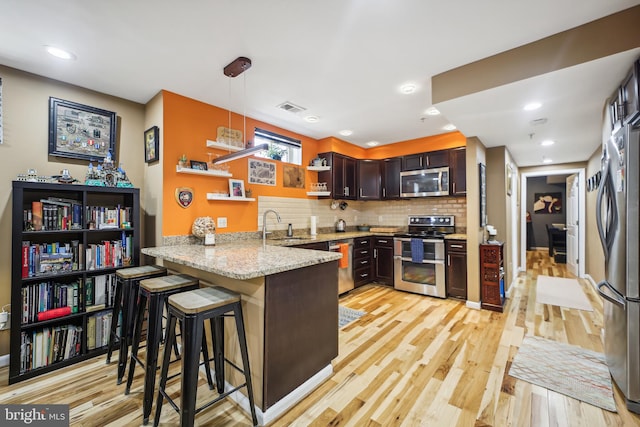 kitchen with light hardwood / wood-style floors, kitchen peninsula, hanging light fixtures, appliances with stainless steel finishes, and light stone countertops