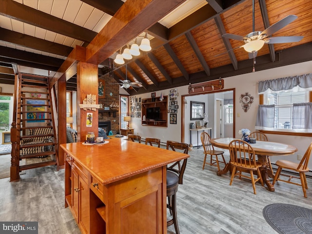 kitchen featuring a brick fireplace, light wood-type flooring, lofted ceiling with beams, and ceiling fan