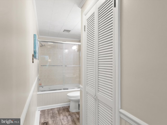 bathroom with ornamental molding, toilet, wood-type flooring, and enclosed tub / shower combo