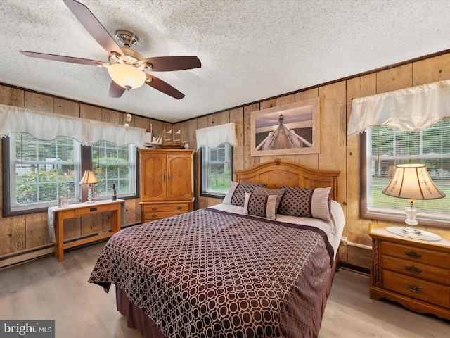 bedroom with a textured ceiling, light wood-type flooring, wooden walls, and ceiling fan