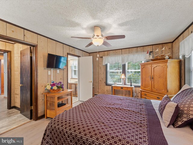 bedroom featuring ceiling fan, a textured ceiling, wooden walls, ensuite bath, and light hardwood / wood-style floors