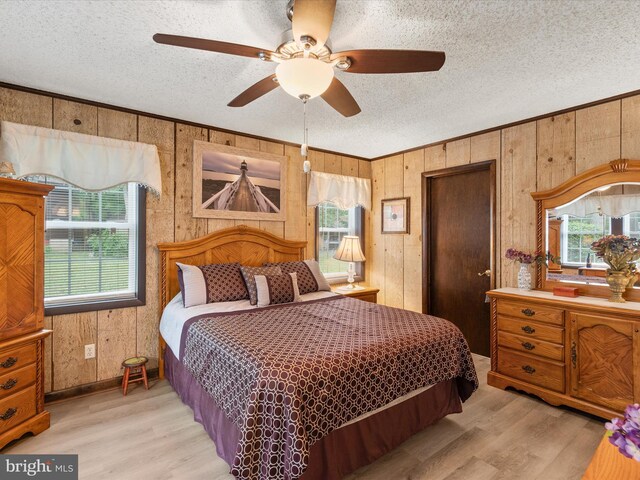 bedroom with wood walls, light hardwood / wood-style floors, a textured ceiling, and ceiling fan