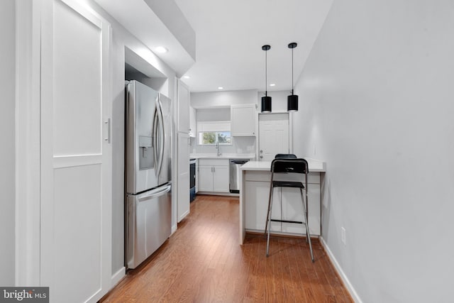 kitchen with white cabinets, hardwood / wood-style floors, appliances with stainless steel finishes, a kitchen bar, and decorative light fixtures