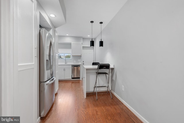 kitchen featuring hardwood / wood-style floors, white cabinets, sink, pendant lighting, and appliances with stainless steel finishes