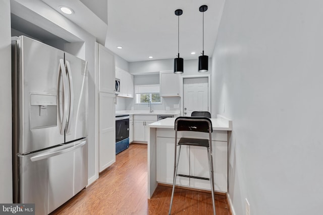 kitchen featuring light hardwood / wood-style flooring, hanging light fixtures, sink, white cabinets, and appliances with stainless steel finishes