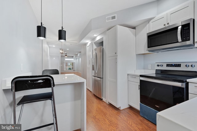 kitchen with white cabinetry, stainless steel appliances, pendant lighting, a notable chandelier, and light hardwood / wood-style flooring