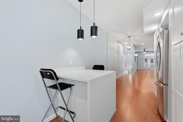 kitchen with kitchen peninsula, light stone counters, stainless steel refrigerator, light hardwood / wood-style floors, and decorative light fixtures