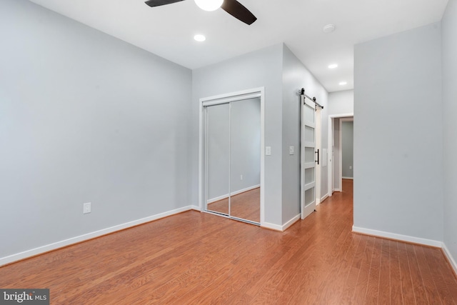 unfurnished bedroom featuring hardwood / wood-style floors, a barn door, a closet, and ceiling fan