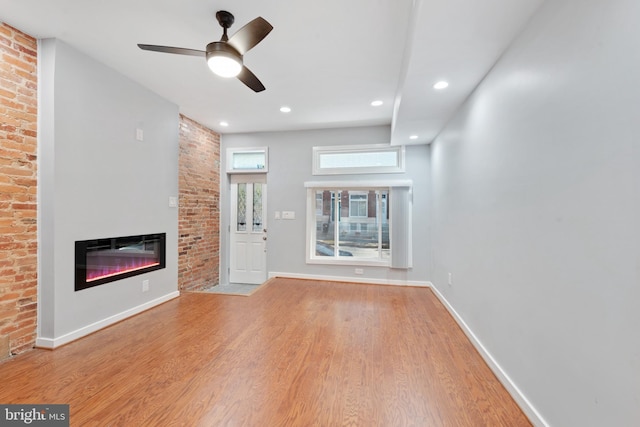 unfurnished living room featuring brick wall, light hardwood / wood-style floors, and ceiling fan