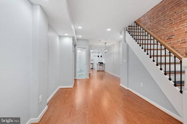 hall with brick wall, a notable chandelier, and light hardwood / wood-style floors