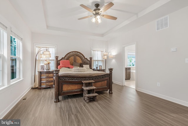 bedroom with ensuite bathroom, hardwood / wood-style flooring, a tray ceiling, and ceiling fan