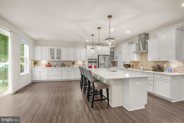 kitchen featuring white cabinets, wall chimney exhaust hood, sink, and a kitchen island with sink