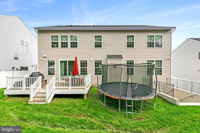 back of property with a deck, a lawn, and a trampoline