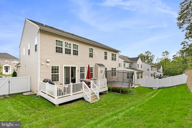 rear view of property featuring a wooden deck, a lawn, and a trampoline