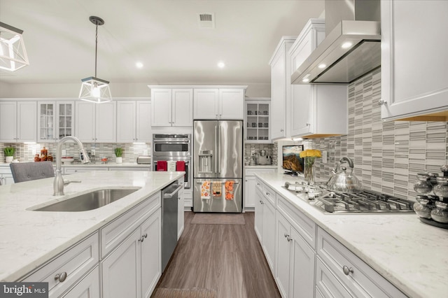 kitchen with wall chimney range hood, white cabinets, stainless steel appliances, and sink