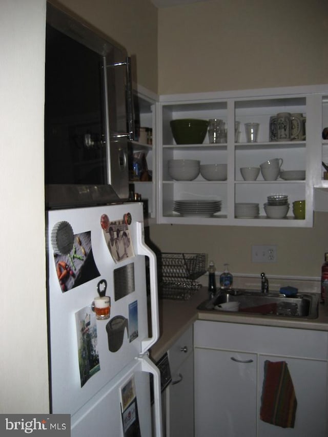 kitchen featuring white cabinets, sink, and white fridge