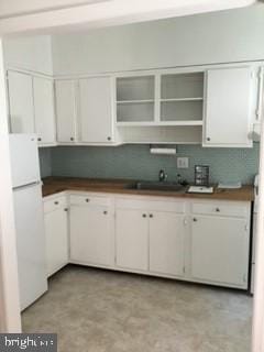 kitchen featuring white refrigerator, sink, tasteful backsplash, and white cabinetry