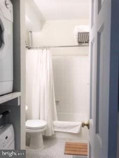 bathroom with stacked washer and dryer, toilet, tile patterned floors, and shower / bath combination with curtain