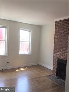 unfurnished living room featuring a brick fireplace, dark hardwood / wood-style floors, and a healthy amount of sunlight