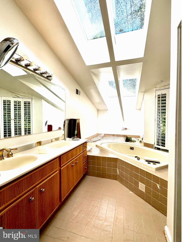 bathroom with vanity, tile patterned floors, a relaxing tiled tub, and a skylight