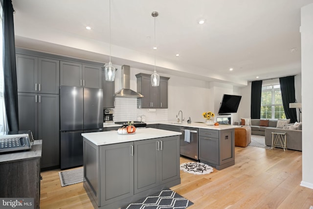 kitchen featuring pendant lighting, gray cabinets, light hardwood / wood-style floors, wall chimney exhaust hood, and appliances with stainless steel finishes