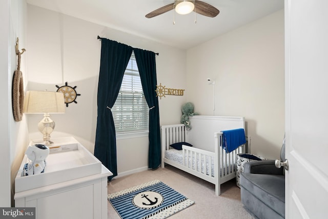 bedroom with ceiling fan, light carpet, and a nursery area