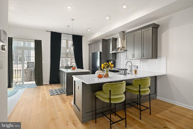 kitchen featuring hanging light fixtures, light hardwood / wood-style floors, wall chimney exhaust hood, fridge, and a center island