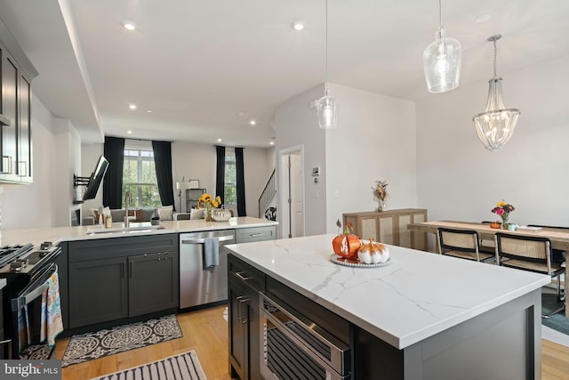 kitchen featuring pendant lighting, sink, stainless steel appliances, a center island, and light hardwood / wood-style floors