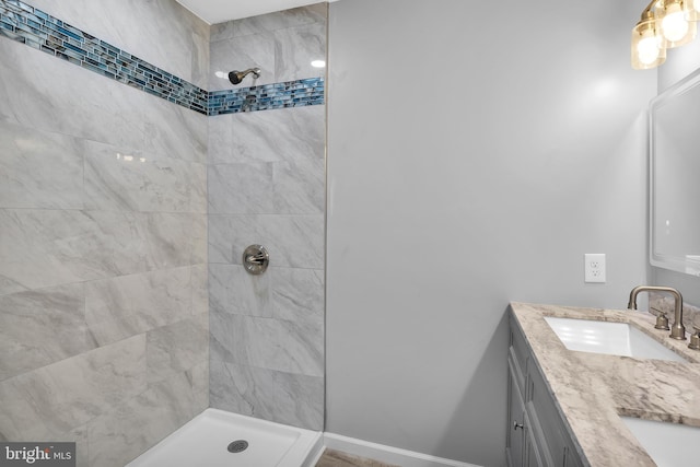 full bath featuring double vanity, tiled shower, a sink, and baseboards