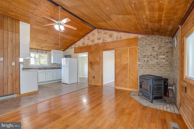 unfurnished living room featuring light wood-type flooring, a wood stove, sink, and wooden walls