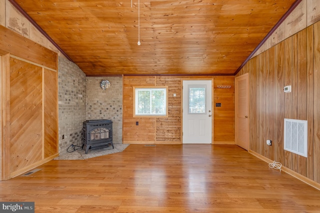 unfurnished living room featuring wood ceiling, wood walls, a wood stove, and light wood-type flooring