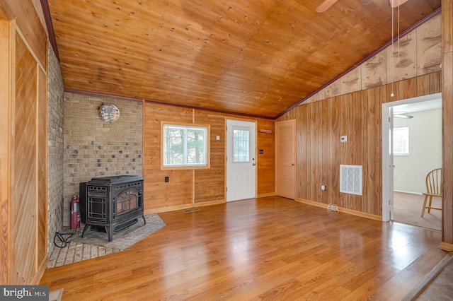 unfurnished living room featuring wood walls, hardwood / wood-style floors, a wood stove, and plenty of natural light